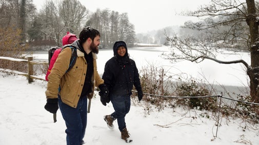 Two parents and a young child stroll through a snowy landscape garden, next to snowy partly frozen water